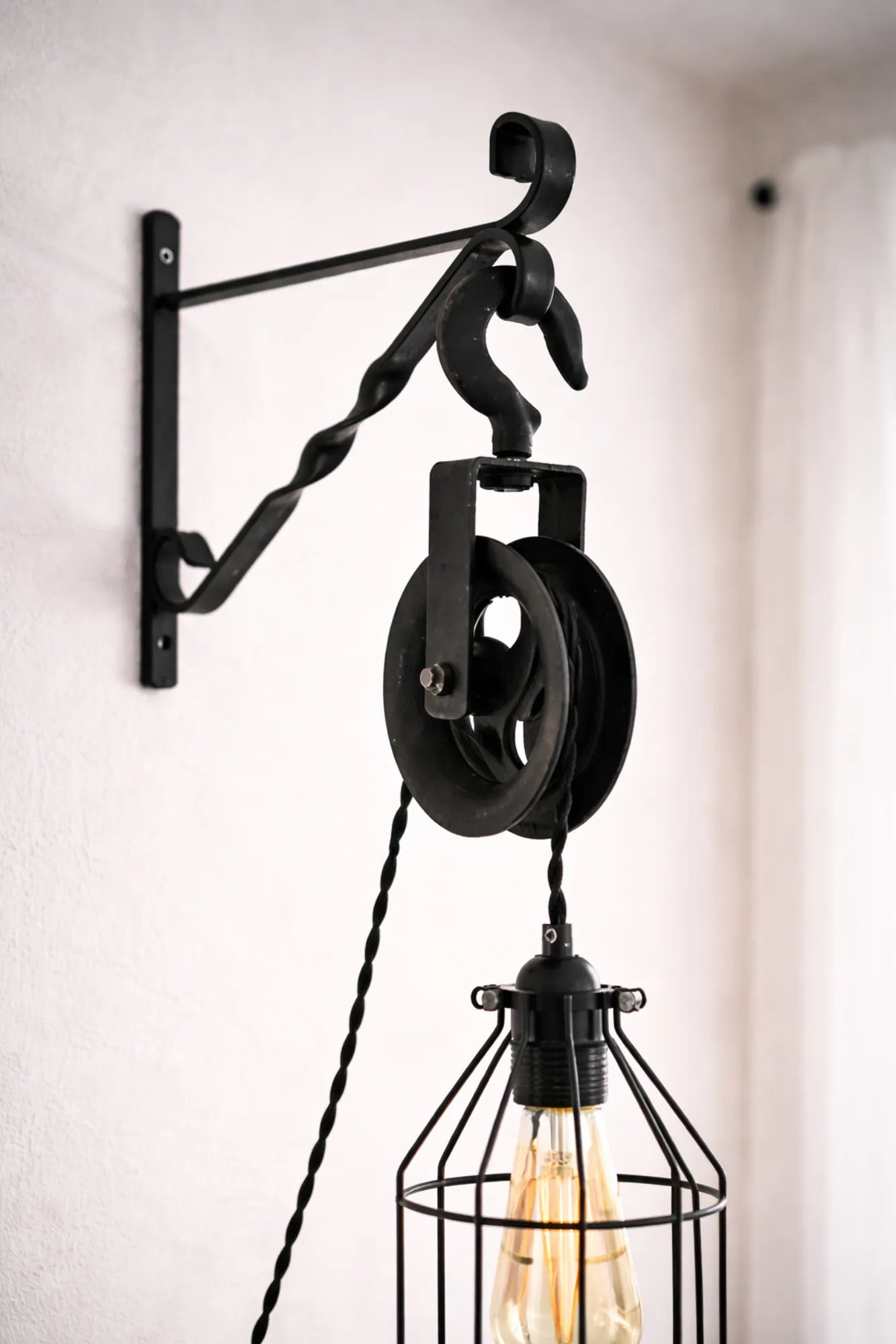 Close-up van zwarte metalen katrol, haak en wandbeugel van industriële wandlamp.