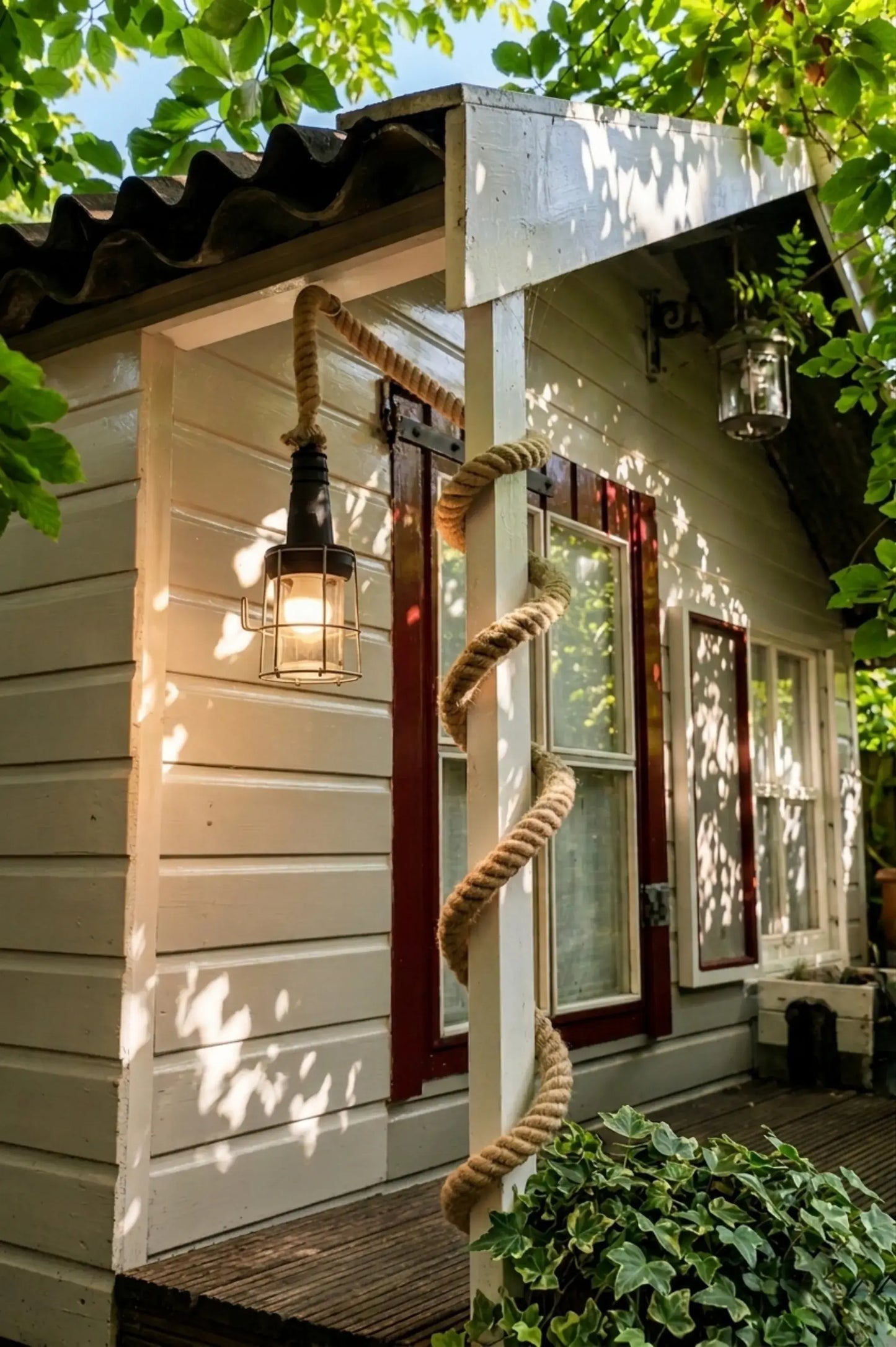 industriële buitenlamp met dik jutetouw en warme verlichting aan houten veranda in groene tuinomgeving